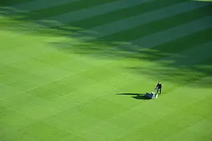 Man mowing a large, striped green lawn under dappled sunlight.